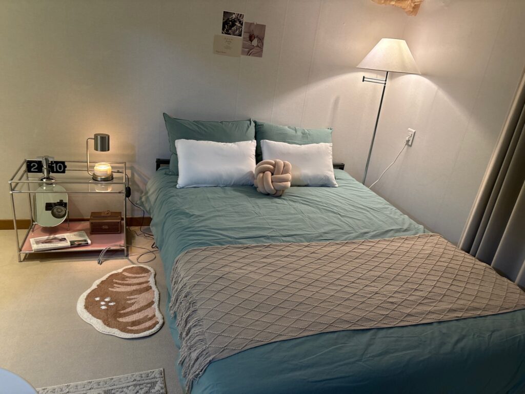 Sage green duvet with beige throw blanket glass side table and pink shelf accent in nature-inspired neutral bedroom design